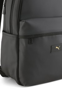 Rucsac negru cu un finisaj neted, mat. Dispune de un logo auriu, compartimente cu fermoar, accente texturate și bretele ajustabile.