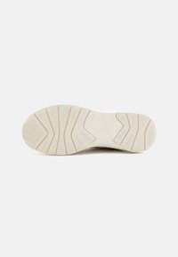 Semelle d'une basket beige avec une semelle à motif et le mot "BOSS" en relief près du centre sur un fond blanc.