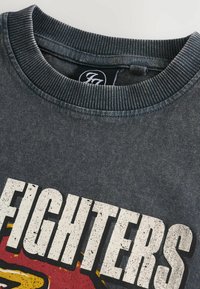 Mörkgr�å sweatshirt med ribbad rund hals, prydd med en djärv grafisk utskrift som står "FIGHTERS" i vitt med färgglada accenter.