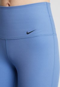 Leggings blu a vita alta realizzati in tessuto elasticizzato, con cuciture piatte e un piccolo logo Nike nero sulla vita.