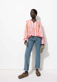 Blouse rayée rose et orange avec un décolleté en V, un ourlet peplum et de longues manches bouffantes, associée à un jean droit bleu clair et des chaussures à imprimé léopard.