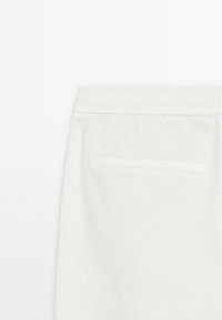 Witte sweats met een elastische tailleband en een enkele achterzak. De stof lijkt zacht met een gladde textuur.