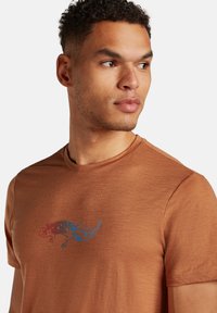 Bruine T-shirt met korte mouwen van lichtgewicht stof, met een kleurrijke hagedisafbeelding op de borst in blauwe en rode tinten.