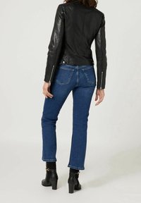 Svart läderjacka med en figurnära design, matchad med blå denimjeans och svarta klackade ankelstövlar. Synlig sömnad och fickdetaljer.