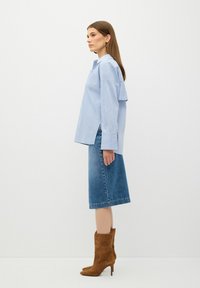 Maglietta a righe blu e bianche con una vestibilità rilassata e fessure laterali, abbinata a una gonna di denim fino al ginocchio e stivali con tacco in suede marroni.