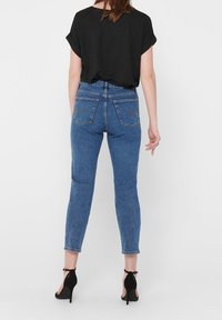 Jeans in denim blu, aderenti, con vita media, tasche posteriori e dettagli di cucitura. Abbinati a una maglietta nera larga e tacchi alti neri.