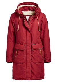 Rode, lange parka met een capuchon, gemaakt van een gestructureerde stof. Beschikt over een schapenvachtvoering, een rits aan de voorkant en twee grote knoopzakken.