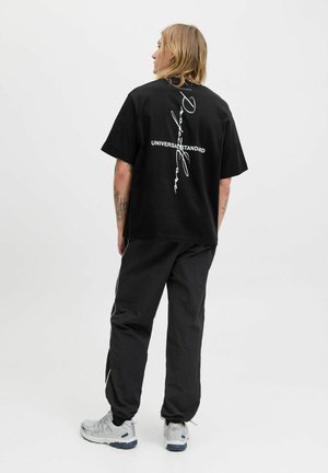 Black cotton t-shirt with white graphic text on the back, paired with black pants and gray sneakers featuring a mesh design.