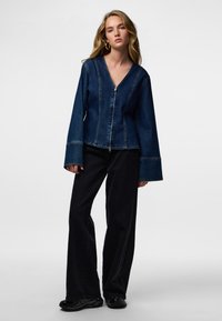 Denimjakk v-kaelusega, lukuga ja laiade varrukatega; sinise kangaga, millel on kontrastõmblused. Sobitatud mustade laiade pükstega.