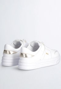 Sneakers bianche con tomaia in pelle liscia, dettagli metallici dorati sul tallone e suola in gomma bianca spessa. Design minimalista senza motivi.