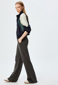 Kleur geblokte windbreaker met marineblauwe, crèmekleurige en groene panelen; slimfit manchetten. Wijde, rechte donkergrijze broeken met zijzakken en een gladde textuur.