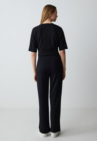 Zwart cropped t-shirt met korte mouwen en een losse pasvorm, gecombineerd met hoge zwarte flared broeken. Beide gemaakt van een zachte, rekbare stof.