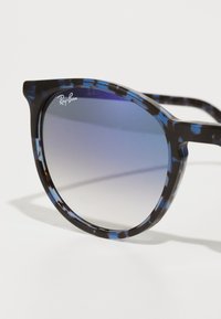 Ochelari de soare Ray-Ban cu un cadru modelat în negru și albastru, formă curbată de cat-eye și lentile gri cu gradient, prezentând logo-ul Ray-Ban.