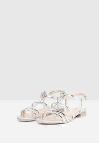 Sandales argentées avec une texture reptilienne, plusieurs brides entrelacées, des accents floraux et un petit talon carré.