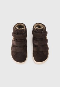 Zapatos de charol marrón de caña alta con dos correas de Velcro y un forro suave y texturizado. Presentan una suela de goma blanca y un diseño de punta redondeada.