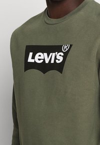 Sweatshirt vert olive en coton, avec un grand logo noir Levi's accompagné de texte blanc et un design classique de col rond.
