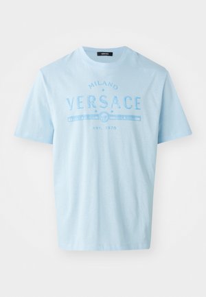 T-shirt en coton bleu clair avec un graphisme texte "MILANO VERSACE" en bleu contrasté, manches courtes et col rond.