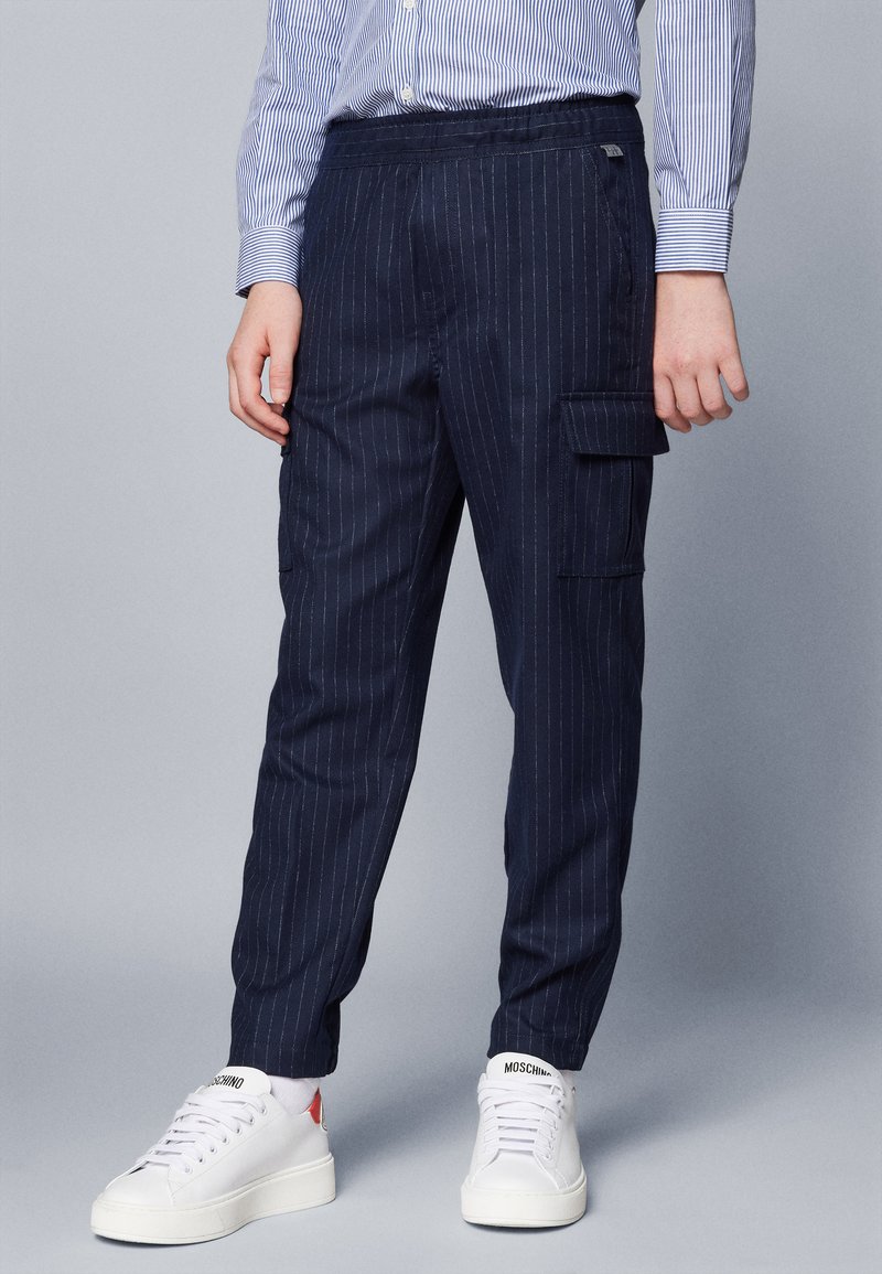 Pantaloni cargo a righe navy con vita elastica, tasche laterali, taglio dritto, abbinati a scarpe da ginnastica bianche. Il materiale sembra leggero e strutturato.