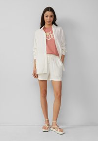 Chemise blanche à texture, t-shirt graphique rose, short blanc à cordon de serrage, et sandales à lanières avec une semelle épaisse.