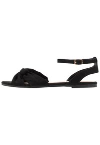 Sandales plates en suede noir avec un design noué à l'avant, une bride de cheville réglable et une semelle en caoutchouc à profil bas.