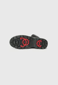 Talpa de pantof negru cu un model de textură, având logo-uri circulare roșii și accente. Fundal alb curat.