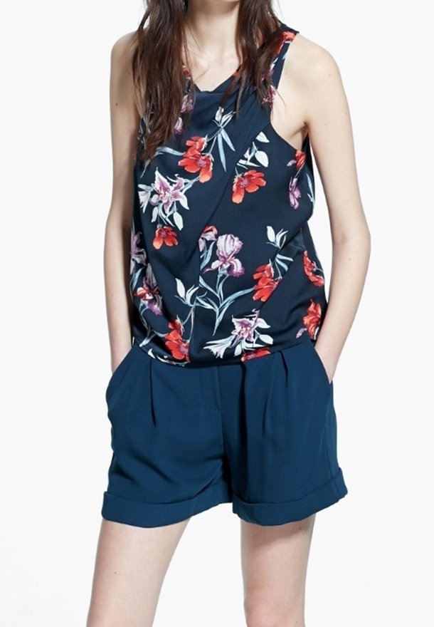 Top in tessuto con stampa floreale blu marino, decorato con fiori rossi e rosa, abbinato a pantaloni shorts blu con risvolti e pieghe frontali. Tessuto dalla consistenza liscia.