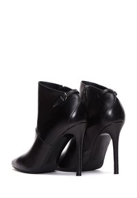 Botas de piel negra hasta el tobillo con punta afilada y tacón alto de aguja. Incluyen cremalleras laterales y una textura suave.