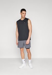 Sort ærmeløs træningsshirt, lysegrå shorts med sort kant, hvide sneakers og hvide sokker med et logo. Enkel design og pasform.
