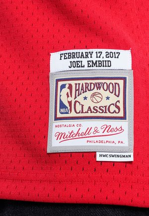 Maillot de basket rouge avec une texture perforée, comportant une étiquette cousue affichant "Hardwood Classics", le nom du joueur et la date.