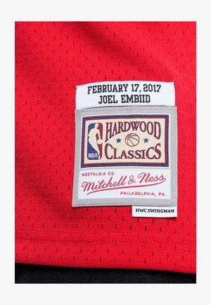 Maillot de basket rouge avec une texture perforée, comportant une étiquette cousue affichant "Hardwood Classics", le nom du joueur et la date.
