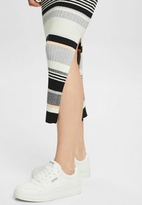 Jupe côtelée rayée avec fente latérale en tons noir, blanc, gris et pêche ; associée à des baskets blanches avec semelles texturées et logo.