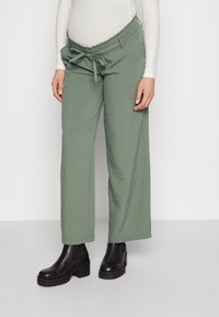 Ljusgrönavida byxor med dragsko i midjan, tillverkade av mjukt tyg, i kombination med svarta ankelstövlar.