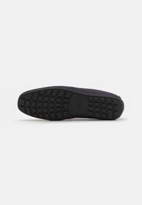 Chaussure en daim avec une semelle en caoutchouc noire. Présente une semelle extérieure plate et texturée avec un motif en grille pour l'adhérence et le support. La tige est de couleur foncée.