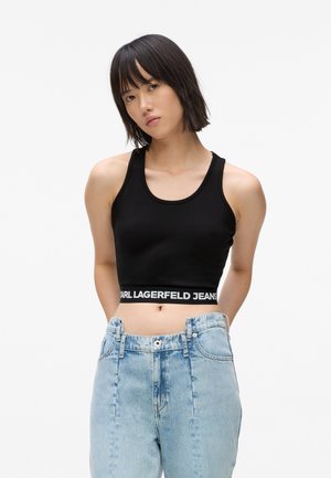 Crna kratka majica s okruglim izrezom i širokim naramenicama. Elastična traka s natpisom "CARL LAGERFELD JEANS". Uparena sa svijetloplavim trapericama visokog struka.