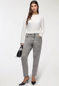 Jeans grigi alti in vita con una vestibilità comoda, tasche frontali e finitura sbiadita, abbinati a un top bianco a maniche lunghe e una borsa nera.