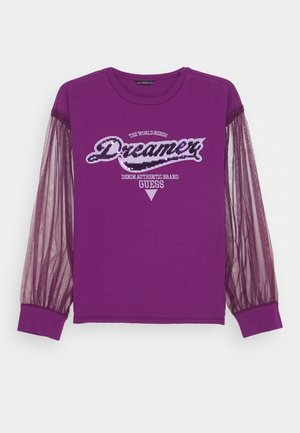 Chemise violette à manches longues avec manches en maille transparente et texte à sequins disant « "Dreamer" » et « "Denim Authentic Brand Guess" » à l'avant.