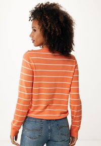 Pomarańczowy sweter w paski z białymi poziomymi liniami, długimi rękawami i okrągłym dekoltem. Posiada guziki na ramieniu.