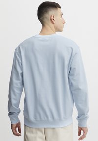 Felpa azzurra chiara con maniche lunghe, polsini e orlo a coste, realizzata in un morbido tessuto; presenta un design sul retro semplice e privo di decorazioni.