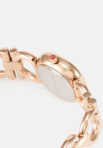 Rose gold watch with a glossy, rounded case, linked chain bracelet, and a small red accent on the side. Smooth metal surface.