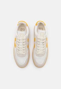 VEJA sneaker fehér bőr felsőrésszel, sárga velúr díszítéssel és bézs hálós részletekkel, gumírozott talppal és kerek fűzőkkel kiegészítve.