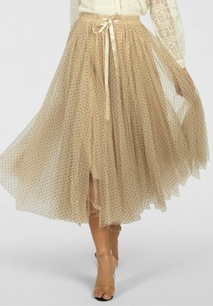 Beiger Tüll-Midirock mit schwarzen Polka Dots, Satinschleife am elastischen Bund, kombiniert mit nudefarbenen High-Heel-Sandaletten mit Knöchelriemen.