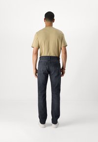 Camisa beige de manga corta combinada con jeans rectos de color azul oscuro. Los jeans cuentan con dos bolsillos traseros y una cinturilla negra.