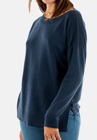 Marinblå tröja med vid halsringning, ribbade muddar och fåll. Har sidoslitsar nertill och ett mjukt, strukturerat tyg.