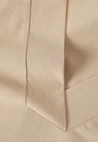 Beige szövet, sima textúrával és finom fényes felülettel, ferde varrással és tiszta szélekkel, elegáns megjelenést kölcsönözve.