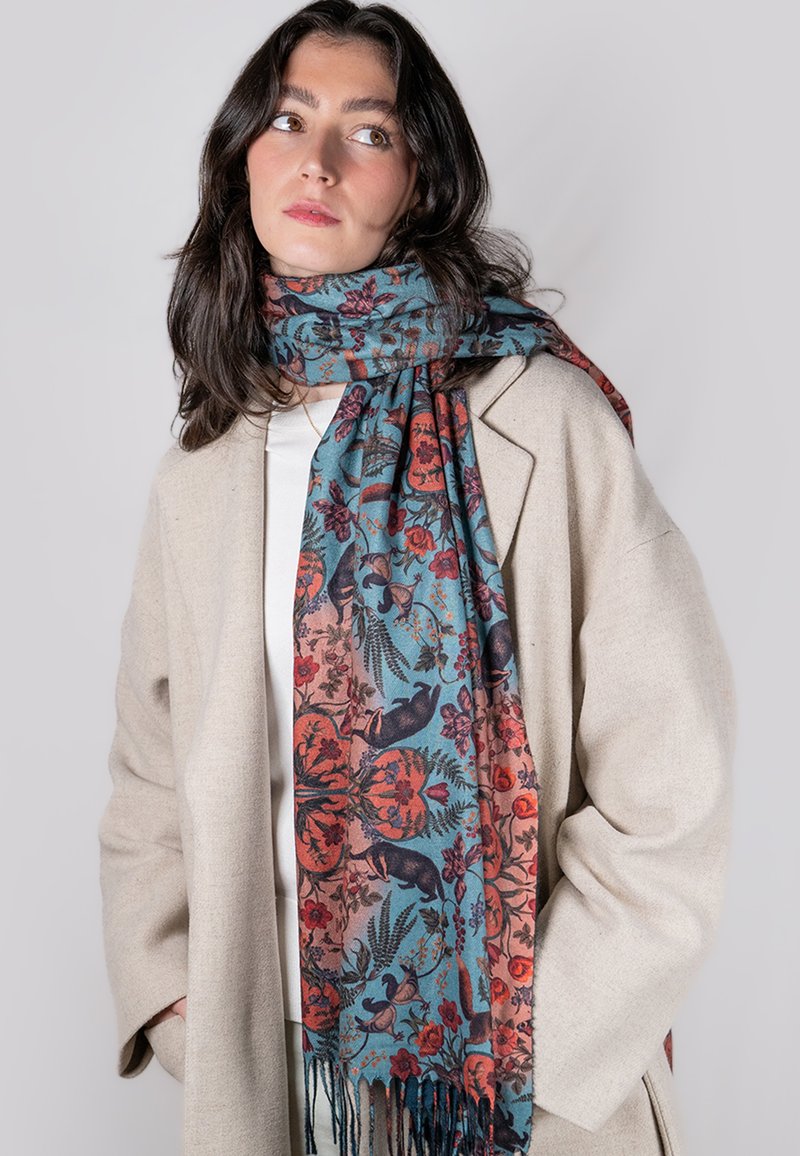 Bufanda con estampado floral en tonos azul verdoso y óxido, fabricada en tejido suave, con bordes con flecos e intrincados motivos animales.
