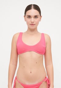 Bikini rose en tissu texturé, avec un haut à larges bretelles et des liens latéraux réglables sur le bas. Design simple sans motifs.