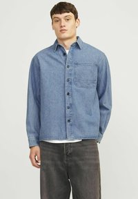 Hele sinine denim särk pikkade varrukatega, nööpidega ees ja rinnataskuga; omab lõppumist ja peent tekstuuri.