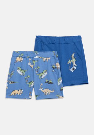 Twee paar kindershorts; één lichtblauw met kleurrijke dinosaurus- en vulkaanprints, de andere effen blauw met een dinosaurus die een camera vasthoudt.