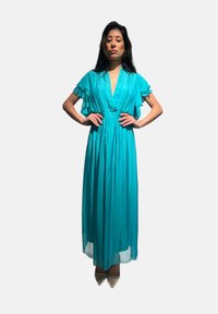 Lungo vestito turchese con maniche a volant corte, scollatura a V profonda e una linea fluida. Tessuto morbido, lungo fino al pavimento, abbinato a scarpe appuntite.