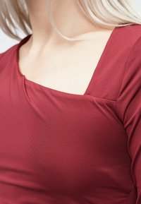 Bordo majica dugih rukava s kvadratnim izrezom, izrađena od glatkog, teksturiranog materijala koji blago rasteže i ima suptilne dijagonalne linije.